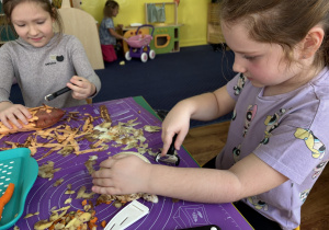 Dzieci siedzą przy stole i obierają warzywa.