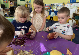 Dzieci siedzą przy stole i obierają warzywa.