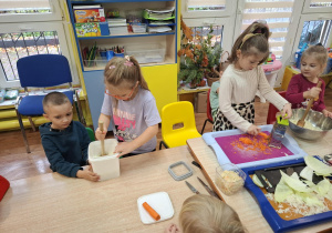 Dzieci ścierają marchewkę i ubijają kapustę.