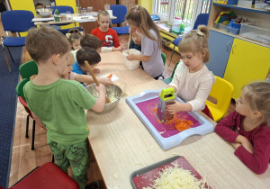 Dzieci ścierają marchewkę i ubijają kapustę.