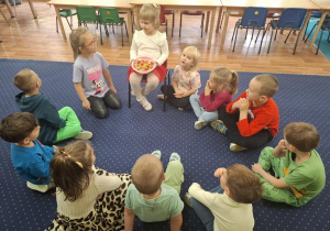 Dzieci siedzą w kole na dywanie.