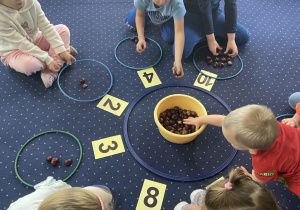 Dzieci siedzą na dywanie i rozwiązują zadania matematyczne.