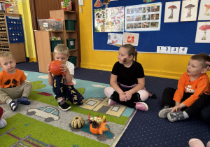 Dzieci siedzą w kole i oglądają dynie.