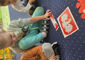 Dzieci siedzą na dywanie i układają godło.