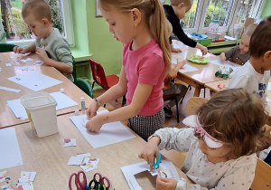 Dzieci siedzą przy stole i wykonują zadanie.