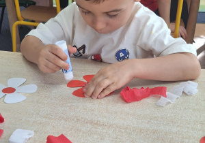 Dzieci siedzą przy stole i wykonują zadanie.