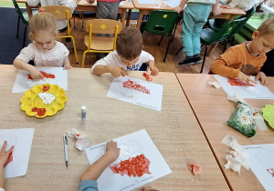 Dzieci siedzą przy stole i wykonują zadanie.