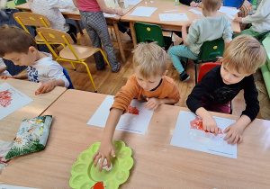 Dzieci siedzą przy stole i wykonują zadanie.