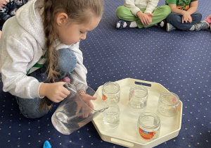 Dziewczynka nalewa wody do słoika.