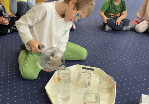 Chłopiec nalewa wody do słoika.