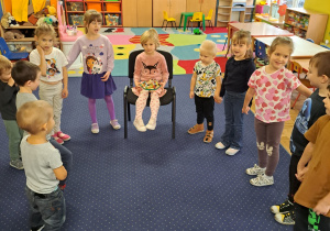 Dzieci stoją w półkolu i śpiewają "100 lat".