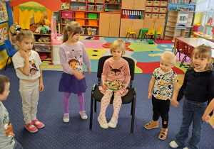 Dzieci stoją w półkolu i śpiewają "100 lat".