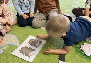 Dzieci siedzą na dywanie w kole i wykonują zadanie.