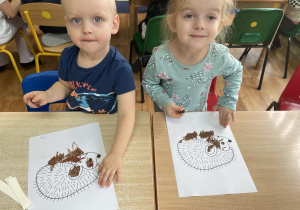 Dzieci siedzą przy stole i wykonują zadanie.