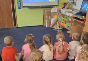 Dzieci siedzą na podłodze i oglądają film edukacyjny.