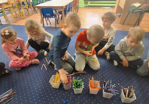 Dzieci siedzą w kole i wybierają kredki.