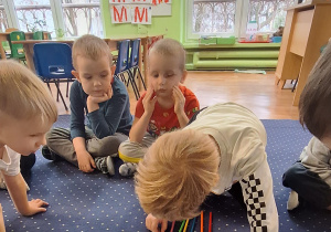 Dzieci siedzą w kole, chłopiec koloruje kredki.