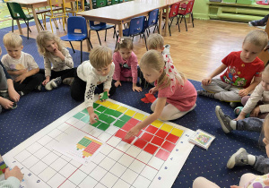 Dzieci siedzą w kole i wykonują zadanie na macie do kodowania.