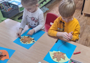 Dzieci siedzą przy stole i wykonują zadanie plastyczne.