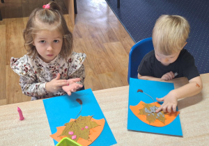 Dzieci siedzą przy stole i wykonują zadanie plastyczne.