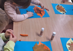 Dzieci siedzą przy stole i wykonują zadanie plastyczne.