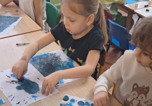 Dzieci siedzą przy stole i wykonują zadanie plastyczne.