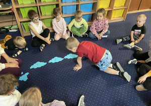 Dzieci siedzą na dywanie i odczytują cyfry z chmurek.