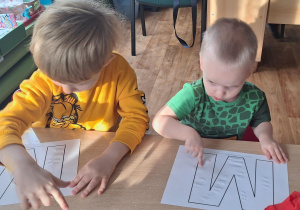 Dzieci siedzą przy stole i wykonują zadanie plastyczne.