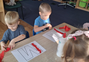 Dzieci siedzą przy stole i wykonują zadanie plastyczne.