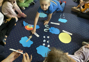 Dzieci siedzą na dywanie i oglądają symbole pogody.