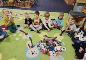 Dzieci siedzą w kole, przed nimi leżą ubranka dla misia.