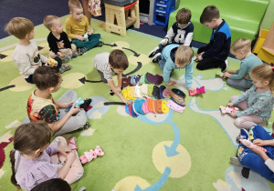 Dzieci siedzą w kole, przed nimi leżą kamizelki dla misia.