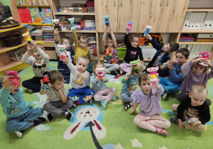 Dzieci siedzą na dywanie i prezentują swoje misie.