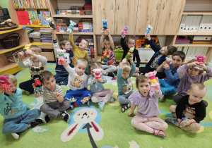 Dzieci siedzą na dywanie i prezentują swoje misie.