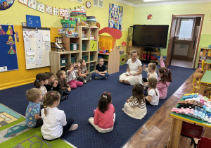 Dzieci siedzą w kole i słuchają panią.