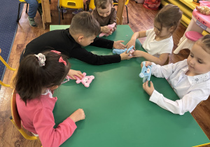 Dzieci siedzą przy stole i oglądają wybranego przez siebie misia.