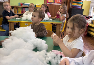 Dzieci siedzą przy stole i wypełniają wnętrze misia.