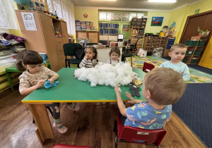 Dzieci siedzą przy stole i wypełniają wnętrze misia.