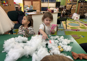 Dzieci siedzą przy stole i wypełniają wnętrze misia.