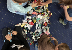 Dzieci siedzą na dywanie i wybierają ubranka dla swojego misia.