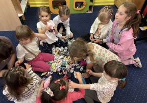 Dzieci siedzą na dywanie i wybierają ubranka dla swojego misia.