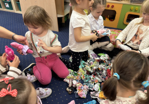 Dzieci siedzą na dywanie i wybierają ubranka dla swojego misia.