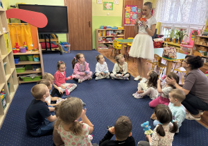 Dzieci siedzą w kole i słuchają pani.