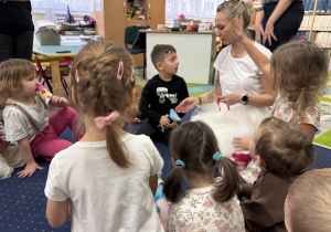 Dzieci siedzą na dywanie i słuchają pani.