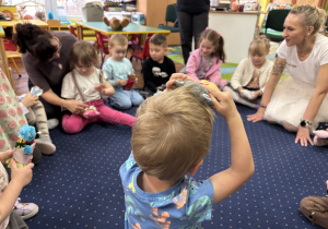 Dzieci siedzą w kole na dywanie i słuchają.