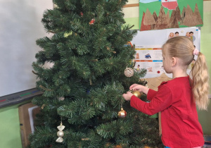Dziewczynka wiesza ozdoby na choince.