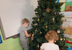 Dzieci wieszają ozdoby na choince.