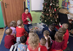 Dzieci siedzą przy choince i pudle z prezentami.