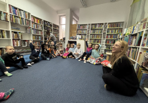 Dzieci siedzą na podłodze i słuchają opowiadania.
