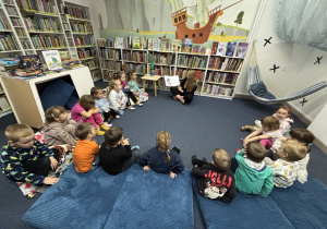 Dzieci siedzą na podłodze i słuchają opowiadania.